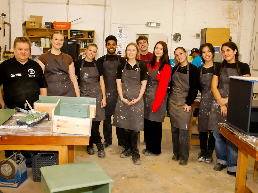 Group of people wearing aprons stand in front of worktops